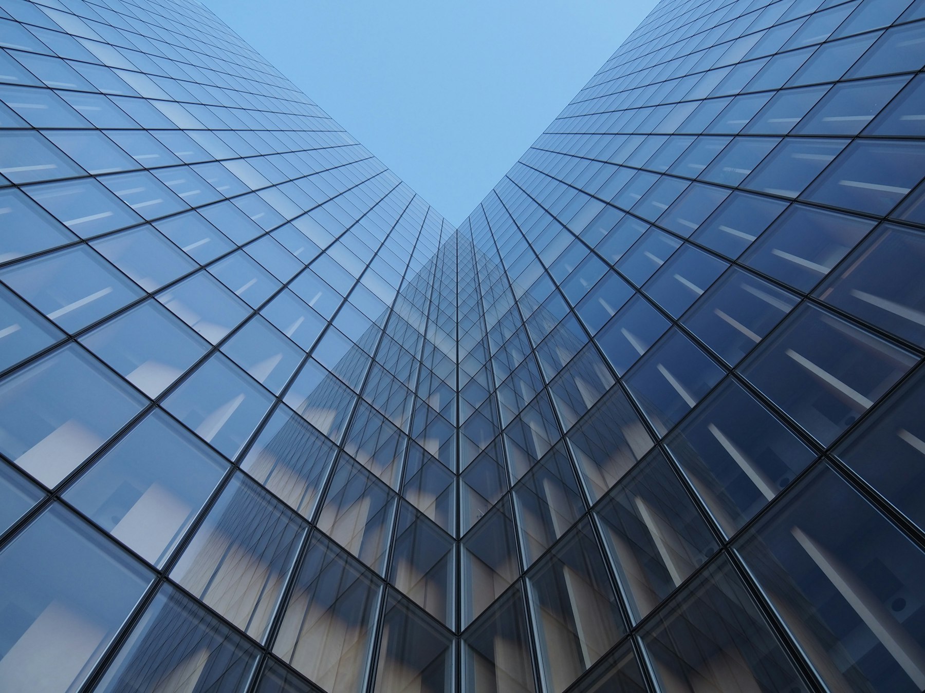 Looking up between two glass towers converging against a clear sky